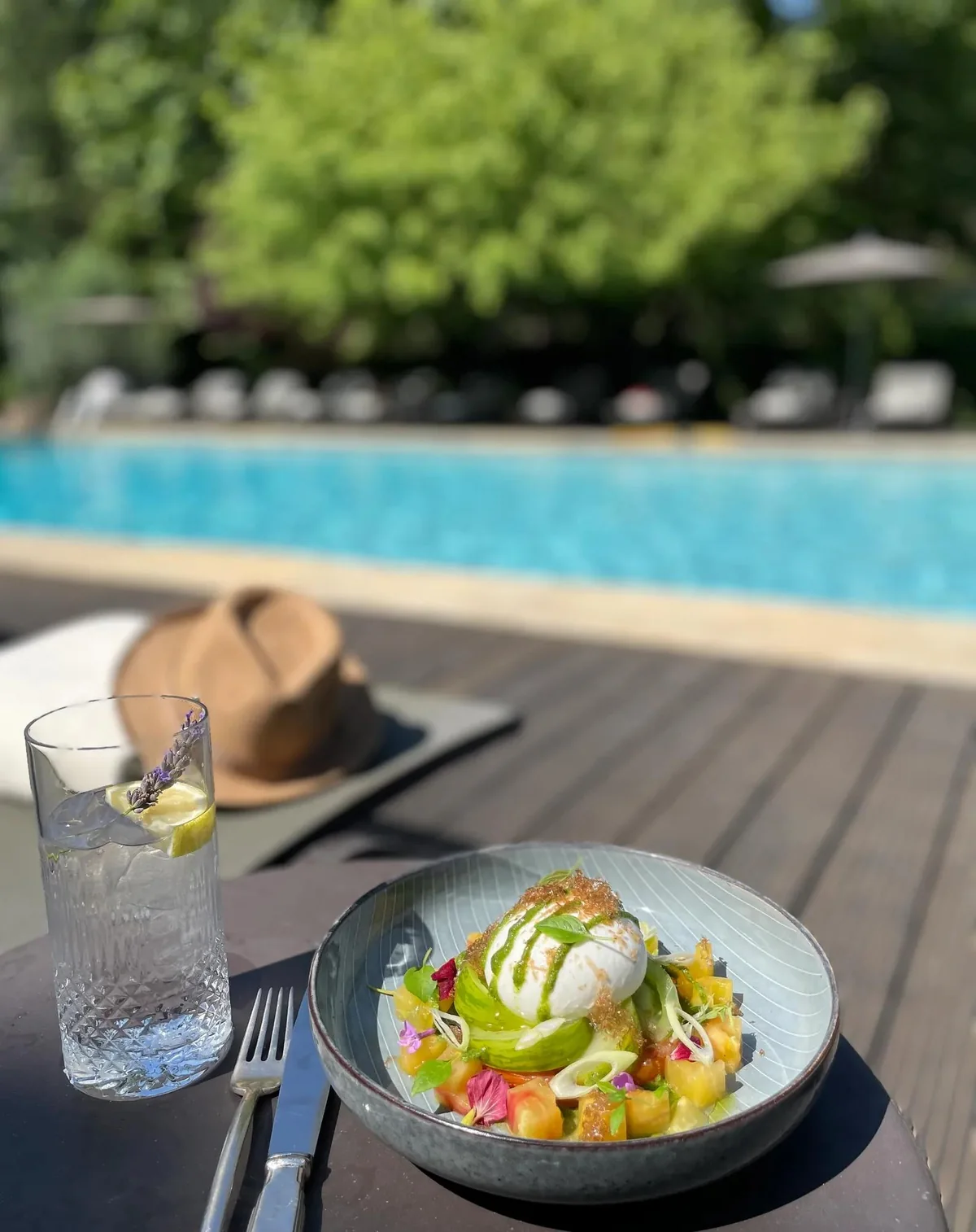 Déjeuner servi au bord de la piscine, chapeau posé sur le transat