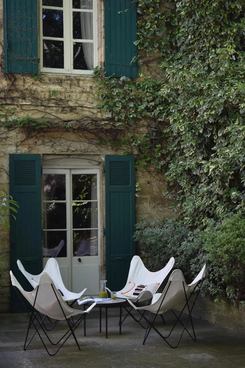Façade du Prieuré aux volets verts, fauteuils blancs dans la cour